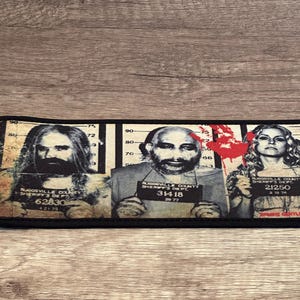 May include: A black rectangular patch featuring three mugshot images with the text "RUGOSVILLE COUNTY SHERIFF'S DEPT" and numbers. A red splatter design is between the second and third mugshots. The text "ZOMBIE GENTLEMAN" is at the bottom.