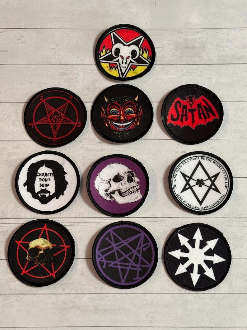 May include: A collection of round, embroidered patches with various occult and gothic designs. The patches feature images of a skull, a devil, a goat head, and pentagrams. Some patches have text, including "Satan" and "Charlie Don't Surf."