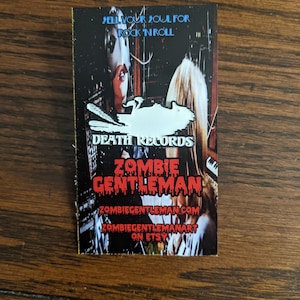 Könnte beinhalten: Rechteckiger Aufkleber mit dunklem Hintergrund, der ein Frauengesicht und den Text "SELL YOUR SOUL FOR ROCK 'N ROLL" zeigt. Der Aufkleber enthält auch den Text "DEATH RECORDS" und "ZOMBIE GENTLEMAN". Zusätzlicher Text lautet "ZOMBIEGENTLEMAN.COM" und "ZOMBIEGENTLEMANART ON ETSY".
