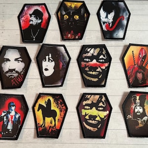 Peut inclure: Plusieurs écussons en forme de cercueil avec des motifs variés, dont un chat noir, des personnages de bandes dessinées et d'autres figures. Les écussons sont de couleurs vives et sont à coudre ou à repasser.