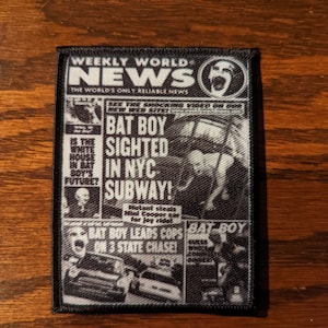 May include: A black and white patch featuring a newspaper front page design. The headline reads "BAT BOY SIGHTED IN NYC SUBWAY!" with other text and images. The patch is rectangular with a black border.