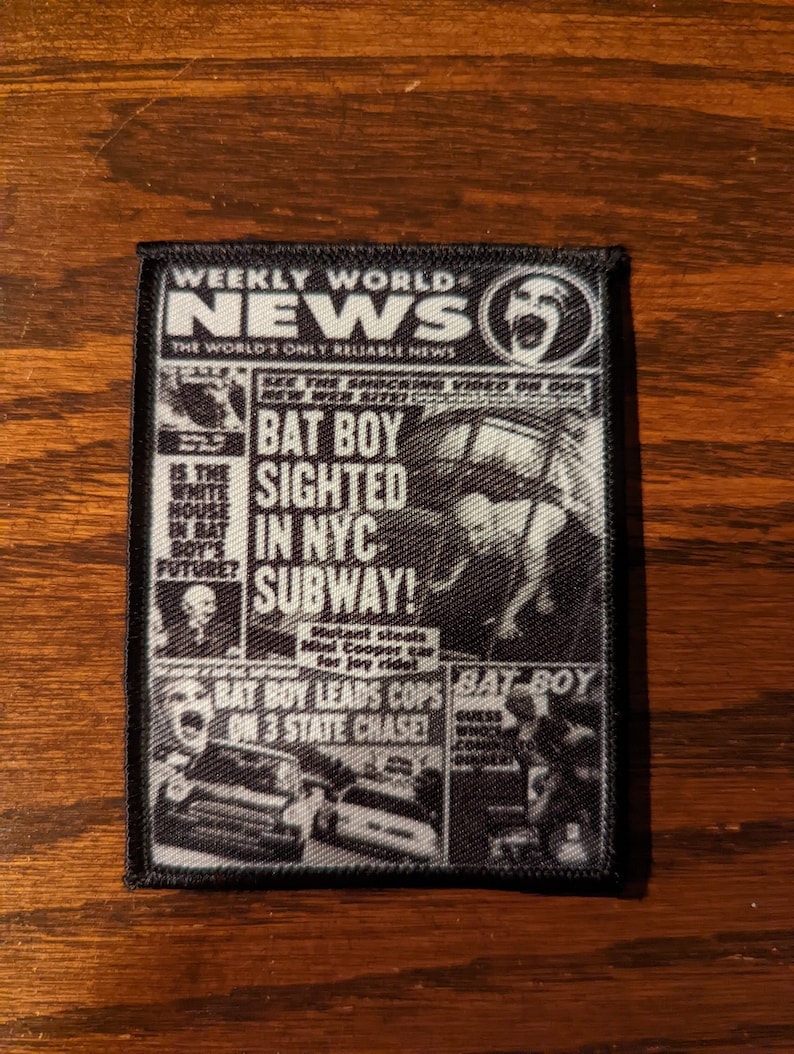 May include: A black and white patch featuring a newspaper front page design. The headline reads "BAT BOY SIGHTED IN NYC SUBWAY!" with other text and images. The patch is rectangular with a black border.