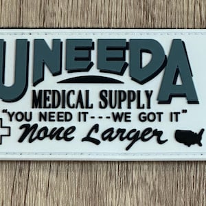 May include: A rectangular patch with the text "UNEEDA MEDICAL SUPPLY" in dark teal and white. The patch includes the phrase "YOU NEED IT---WE GOT IT" and a medical cross symbol. A map of the United States is also included.