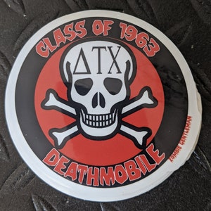 Può includere: Adesivo rotondo con un teschio e ossa incrociate. Il testo "CLASS OF 1963" è rosso, e "DEATHMOBILE" è bianco. Le lettere "ATX" sono sopra il teschio. Sfondo bianco e bordo nero.
