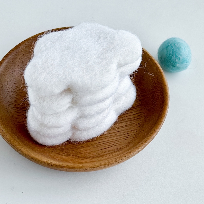 May include: A stack of white felt cloud shapes in a wooden bowl.