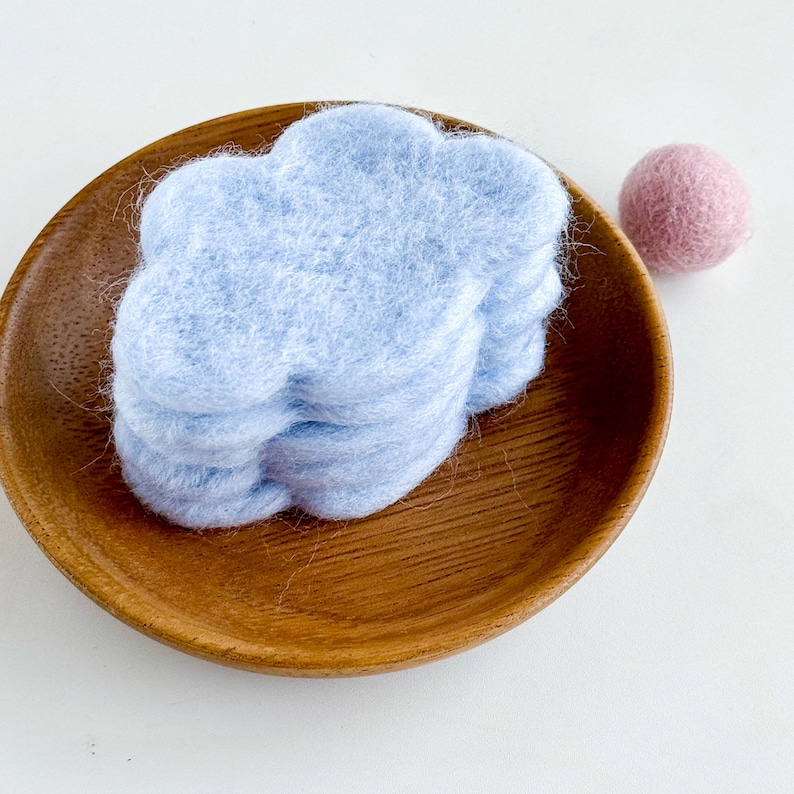 May include: A stack of four light blue felt cloud shapes in a wooden bowl.