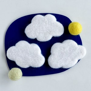 May include: Three white felt clouds on a dark blue background with two yellow felt circles.