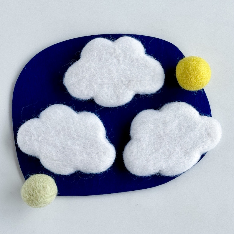 May include: Three white felt clouds on a dark blue background with two yellow felt circles.