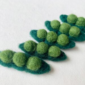 May include: Five felt pea pods with green felt peas inside. The pea pods are arranged in a row, with the largest pod at the bottom and the smallest pod at the top.