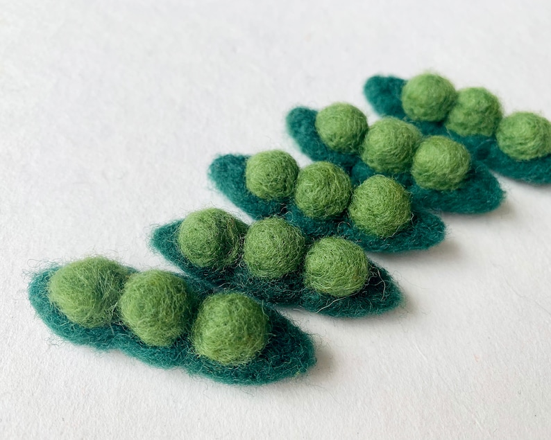 May include: Five felt pea pods with green felt peas inside. The pea pods are arranged in a row, with the largest pod at the bottom and the smallest pod at the top.