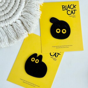 May include: Two black cat embroidery patches with yellow eyes on yellow cards. The cards have the text "BLACK CAT EMBROIDERY PATCH" and "CAT EMBROIDERY PATCH". The cards also have the text "I hope that the world will become more beautiful because of you."