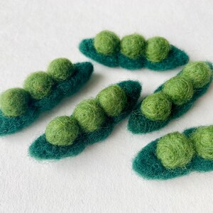 May include: Five felt pea pods with green felt peas inside. The pea pods are a dark green color and the peas are a lighter green color.