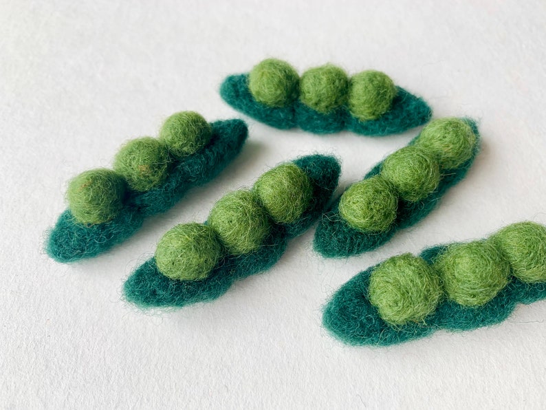 May include: Five felt pea pods with green felt peas inside. The pea pods are a dark green color and the peas are a lighter green color.