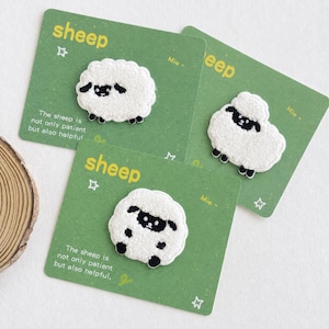 Puede incluir: Tres parches bordados de ovejas blancas y negras sujetos a tarjetas rectangulares verdes individuales. Cada tarjeta presenta el texto "sheep" y "The sheep is not only patient but also helpful." junto con pequeños iconos de estrellas y "Mie ~".