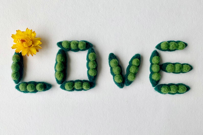 May include: The word "LOVE" spelled out using green felt pea pods. A yellow felt flower is in the upper left corner of the image.