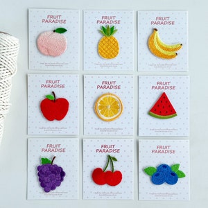 以下が含まれることがあります： 異なる果物をモチーフにした刺繍アイロン接着パッチ9枚セット。桃、パイナップル、バナナ、リンゴ、レモン、スイカ、ブドウ、チェリー、ブルーベリーなど。各パッチには、果物の画像の上に「Fruit Paradise」の文字が書かれています。