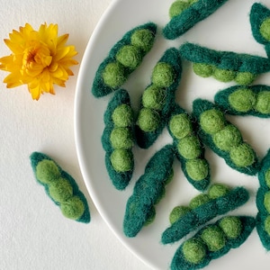 May include: A white plate with green felt pea pods arranged in a decorative pattern. The pea pods are made of felt and have a realistic appearance.