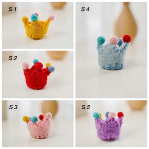 May include: Five small felt crowns labeled S1 through S5. S1 is yellow, S2 is red, S3 is light pink, S4 is light blue, and S5 is purple. Each crown features a scalloped top edge decorated with small, multi-colored felt pom-poms in various colors.