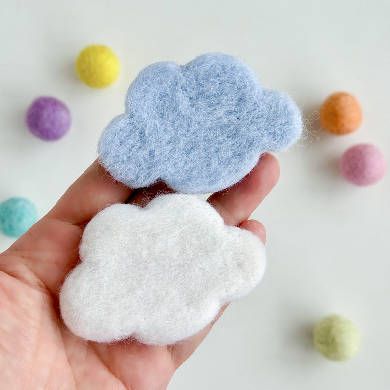 May include: Two felt clouds, one light blue and one white, in the shape of a cloud. The clouds are held in a hand.
