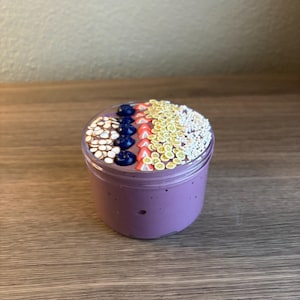 May include: A clear plastic jar filled with purple slime, topped with decorative polymer clay slices shaped like white coconut chips, dark blue blueberries, red strawberry wedges, yellow lemon slices, and small white sprinkles.