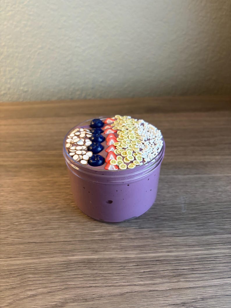 May include: A clear plastic jar filled with purple slime, topped with decorative polymer clay slices shaped like white coconut chips, dark blue blueberries, red strawberry wedges, yellow lemon slices, and small white sprinkles.
