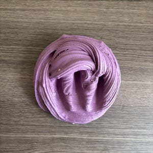 May include: A mound of lavender-colored slime with a thick, pliable, and glossy texture. The substance features deep, swirling ridges and folds across its surface, creating a dense, circular shape with a soft, matte-like appearance.