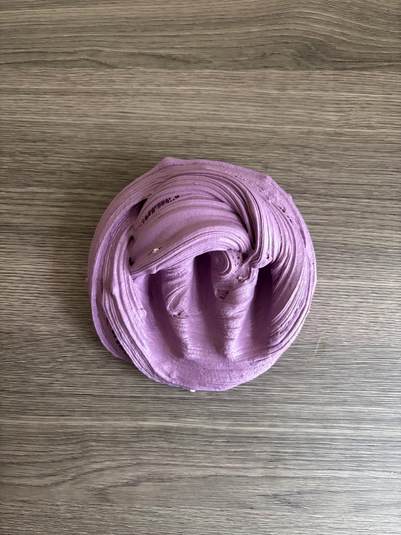 May include: A mound of lavender-colored slime with a thick, pliable, and glossy texture. The substance features deep, swirling ridges and folds across its surface, creating a dense, circular shape with a soft, matte-like appearance.