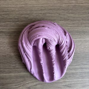 May include: A mound of light purple slime with a thick, textured consistency. The surface features deep, swirling ridges and elongated indentations that create a layered, malleable appearance across the entire circular-shaped mass of material.