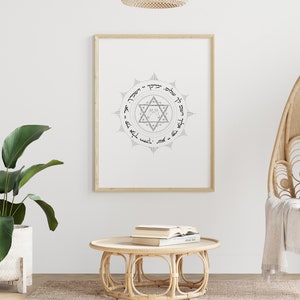 May include: A framed print featuring a black and white illustration of a Star of David with Hebrew text surrounding it. The print is hanging on a white wall above a wicker coffee table with books on top.
