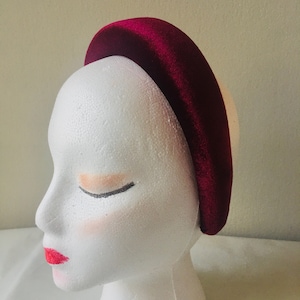May include: A wide, padded headband made of burgundy velvet. The headband is shown on a white mannequin head.