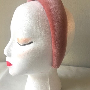 May include: A wide, blush pink velvet headband. The headband is thick and has a smooth, soft texture.