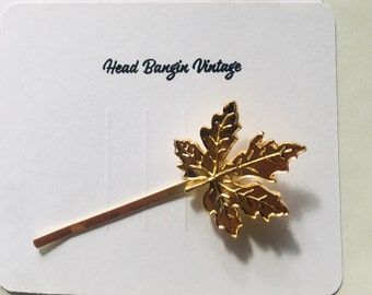 May include: Gold-toned hair clip featuring a maple leaf design. The clip is on a white card with the text "Head Bangin Vintage".