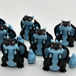 May include: A group of ten small, black and blue dragon figurines with red eyes. The dragons are standing on a white surface.