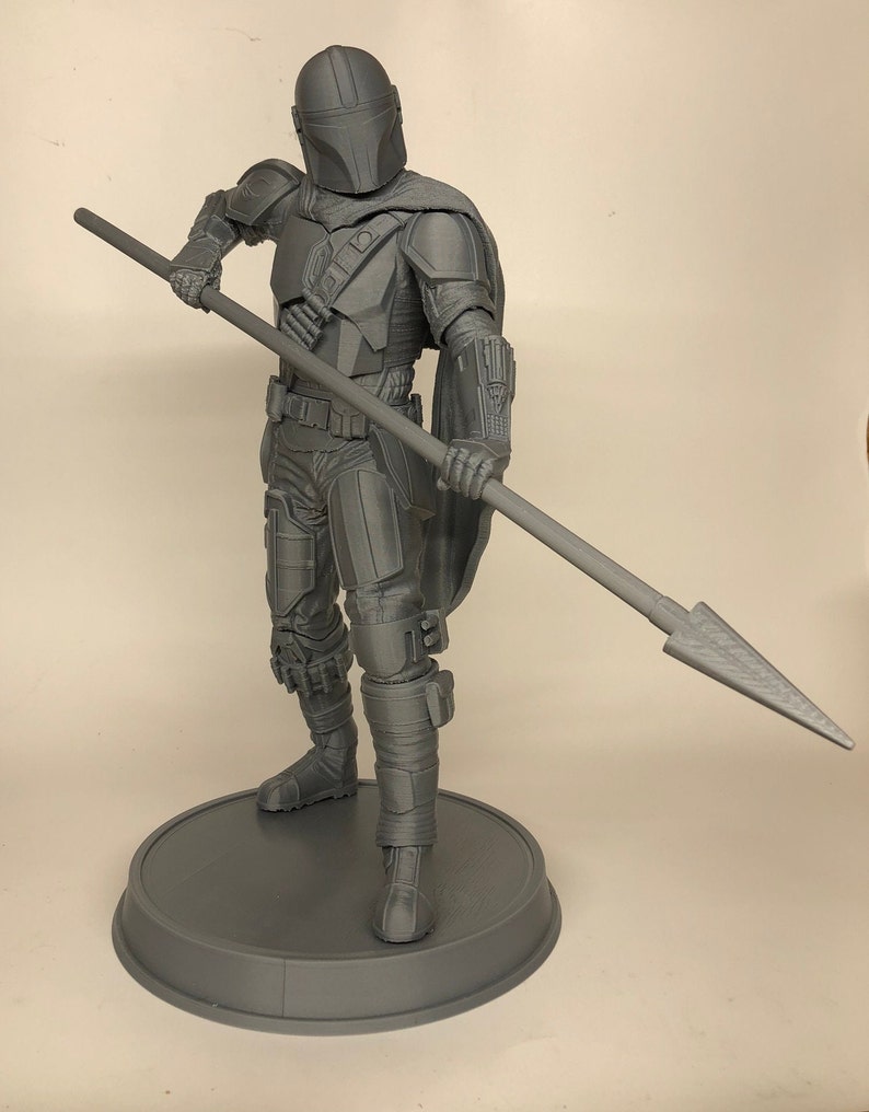 Puede incluir: Una figura de acci&oacute;n gris impresa en 3D de un guerrero mandaloriano sosteniendo una lanza. La figura est&aacute; de pie sobre una base redonda.