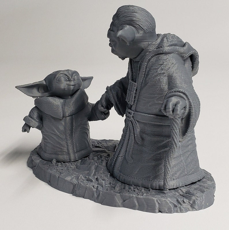 Peut inclure: Une figurine en 3D imprim&eacute;e en gris de Yoda et un jeune Yoda marchant ensemble. Les figurines sont sur une base grise.