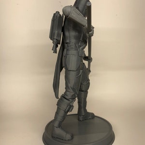 Puede incluir: Una figura gris impresa en 3D de un personaje de una pel&iacute;cula o serie de ciencia ficci&oacute;n. El personaje lleva una capa con capucha y sostiene un bast&oacute;n. La figura est&aacute; de pie sobre una base redonda.