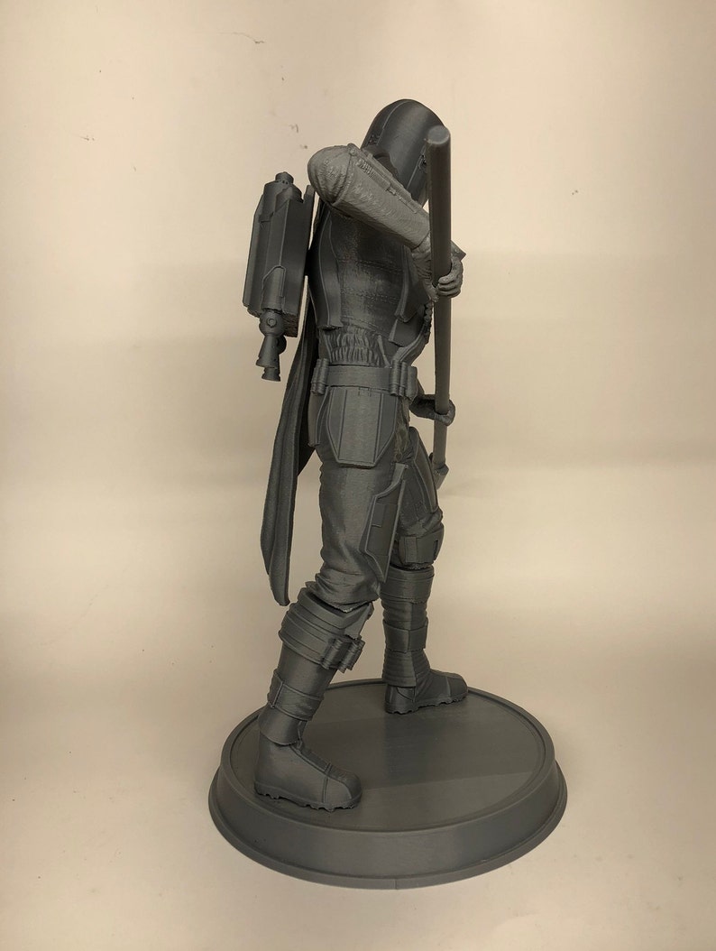 Puede incluir: Una figura gris impresa en 3D de un personaje de una pel&iacute;cula o serie de ciencia ficci&oacute;n. El personaje lleva una capa con capucha y sostiene un bast&oacute;n. La figura est&aacute; de pie sobre una base redonda.
