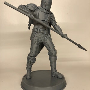 Puede incluir: Una figura gris impresa en 3D de un personaje del universo de Star Wars, sosteniendo una lanza. La figura est&aacute; de pie sobre una base redonda.