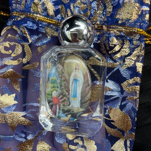 May include: A clear glass bottle with a silver lid containing a small image of the Virgin Mary. The bottle is sitting on a blue and gold fabric.
