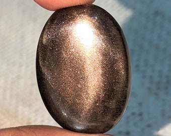 May include: A large, oval-shaped, golden sunstone cabochon with a shimmering, iridescent sheen.