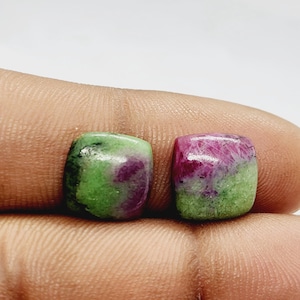 Könnte beinhalten: Zwei quadratisch geschliffene Edelsteine mit einer Mischung aus grünen und magentafarbenen Farben. Die Steine sind glatt und poliert, mit einer leicht abgerundeten Form. Die Edelsteine werden wahrscheinlich für die Schmuckherstellung verwendet.