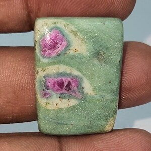 May include: A green and pink gemstone with a square shape. The gemstone has a speckled green background with pink inclusions.