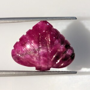 May include: A carved pink ruby gemstone in the shape of a heart. The gemstone is set in a silver tone setting.