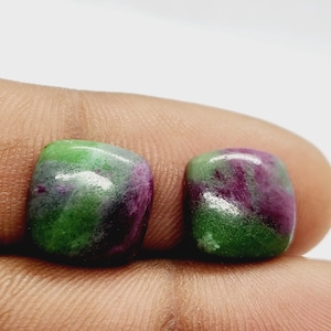 Könnte beinhalten: Zwei quadratisch geschliffene Edelsteine mit einer Mischung aus grünen und tiefroten Farbtönen. Die Steine haben eine polierte, glänzende Oberfläche, und die Farben verschmelzen zu einem marmorierten Effekt. Die Edelsteine werden wahrscheinlich für Schmuck oder andere dekorative Zwecke verwendet.