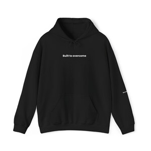 Könnte beinhalten: Schwarzer Kapuzenpullover mit dem Aufdruck "Built to overcome" in Weiß auf der Vorderseite.