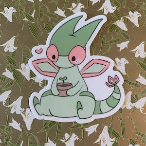 Puede incluir: Una criatura de dibujos animados verde y rosa con ojos grandes y alas que sostiene una pequeña planta en maceta. La criatura tiene un corazón sobre su cabeza y una pequeña cola con una flor en el extremo.