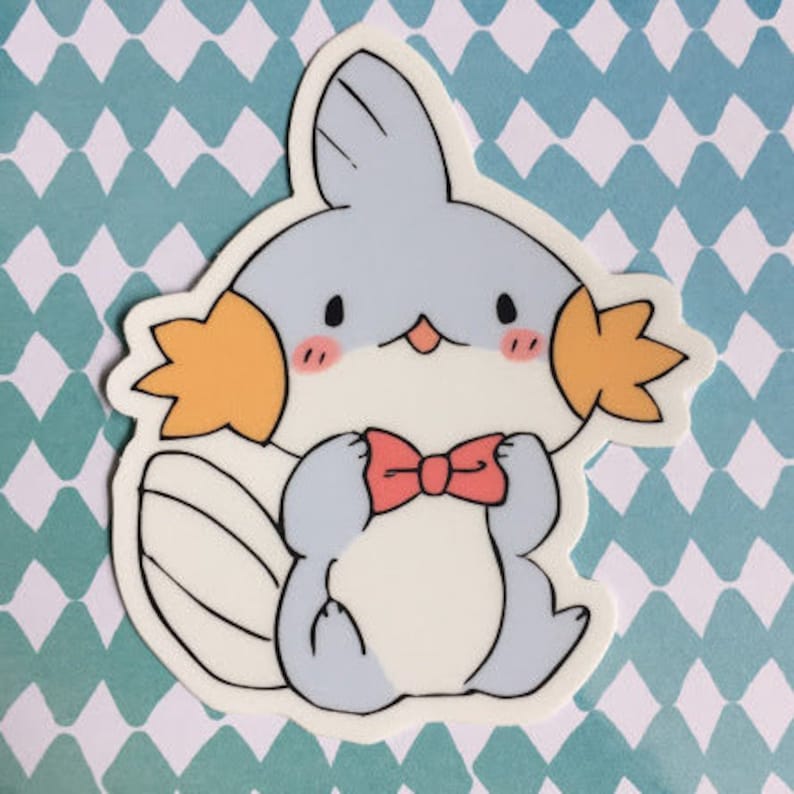 May include: A cartoon sticker of a light blue and white fish with orange fins and a red bow tie. The fish has a cute, cartoonish expression.