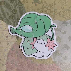 May include: A white cartoon character with a pink flower on its head is holding a green leaf over its head. The leaf is dripping with water.