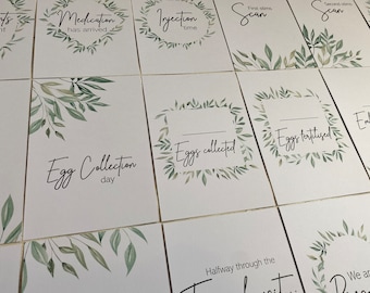 May include: A set of ten printable cards with a leafy green border and white background. The cards feature text such as "Medication has arrived", "Injection time", "First stim scan", "Second stim scan", "Egg collection day", "Eggs collected", "Eggs fertilized", "Halfway through the", and "We are".