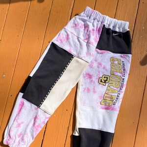 Può includere: Pantaloni della tuta rosa, bianchi e neri con un logo "Colorado" dorato e il testo "Anschutz Medical Campus".